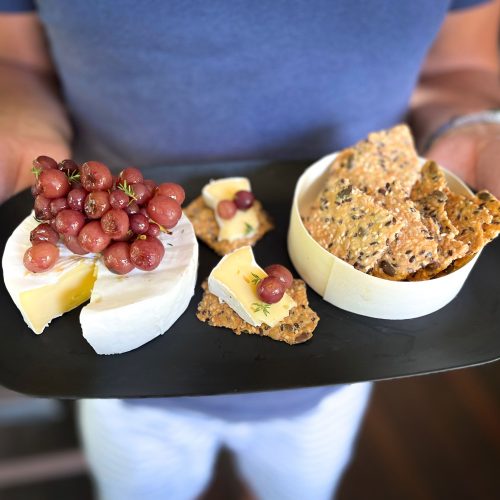Brie cheese and crackers on a plate with roasted grapes held by a man