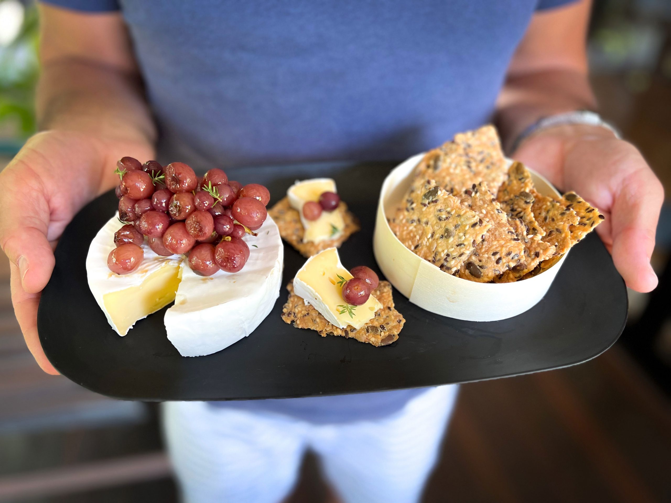 Brie cheese and crackers on a plate with roasted grapes held by a man